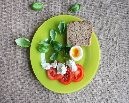 Cooked eggs served on a ceramic plate next to a slice of whole wheat bread